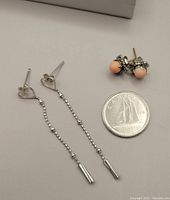 Both pairs of earrings displayed next to a Canadian dime for scale. Long dangle earrings with open heart shapes are visible along with coral stud earrings with pinkish stones.
