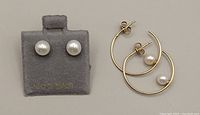 Pair of pearl stud earrings on display card and gold open hoop earrings with pearls on flat surface