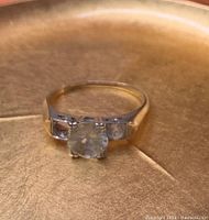 Front view of gold ring showing large central setting with missing stone and two smaller stones on the sides.