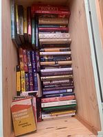 View down into wooden trunk showing stack of assorted hardcover and paperback books organized in rows highlighting the depth and condition of the collection.