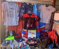 Photo showing multiple boys' clothing items hanging and laid out, including Star Wars jerseys, Under Armour shirts, and Polo Ralph Lauren shirt, along with pool float and slippers.