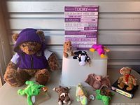 Nine Beanie Babies plush animals with tags displayed on a table with inspirational canvas art behind them