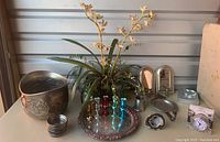 Full lot showing faux floral arrangement in silver planter, pewter cup, shot glasses on a silver tray, glass and silver coasters, wall candleholders, a natural geode rock, and boxed crystal clock.