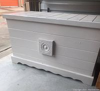Front and side view of white wooden storage trunk showing horizontal plank design, decorative square accents and scalloped base