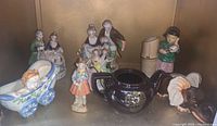 Photo of collectible Japan made figurines arranged together including various human figures, an elephant planter, a teapot and a child in a pram figurine.