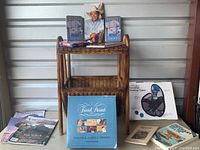 Rattan magazine table showing multiple vintage magazines on lower shelf, framed George Strait tribute standing on middle shelf, and boxed Trivia Pursuit game and book placed beside it.