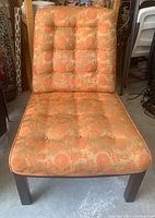 Front view of the chair showing floral orange and beige tufted upholstery with matching buttons on seat and back, wooden legs visible.
