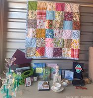 Full view of quilt hanging with items displayed underneath including cup and saucer, figurine, books, candle, glasses, and eyeglasses box.