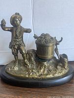 Front view of the vintage bronze farmer inkwell with figure, grape basket ink holder, dog, and black marble base.