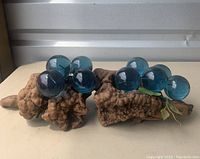 Two vintage 1970s table decor pieces shown side-by-side. Each features natural driftwood bases with clusters of blue lucite balls and green artificial leaves.