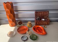 Front image showing large orange glazed vase, orange ceramic trays, coasters, brass clock, rattan basket and small decorative items