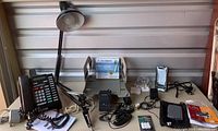 Desk clamp lamp with adjustable arm, black metal; two telephones with cords; CPU caddy; PDA devices and accessories on table