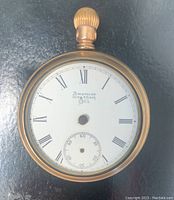 Front view of American Waltham & Co pocket watch showing white dial with Roman numerals and seconds subdial, brand name visible.
