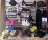 Full view of metal shoe rack showing variety of shoes, slippers, hats, gloves, and accessories arranged on and around the rack.