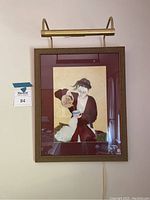 Full frontal view of framed artwork hanging on cream wall with brass picture light above.