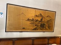 Four-panel Asian artwork mounted on wall showing a mountainous landscape with trees and water, framed with dark thin border.