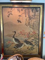 Full view of the Asian style silk and paper watercolor painting framed with wood and brushed gold paint, showing a nature scene with birds and foliage.