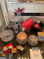 Overview of lot showing acrylic canisters, perfume atomizer, red makeup bag, glass jars, clock, and crystal ashtray on countertop.