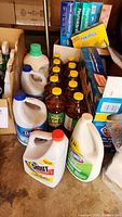 Photo displaying various cleaning bottles including Clorox, Pine-Sol, and Shout along with several boxed kitchen supplies.