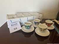 Four espresso cups and saucers arranged on table with packaging in background