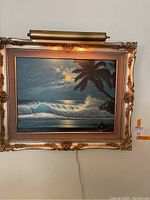 Frontal view of framed oil painting with beach scene and art lamp attached