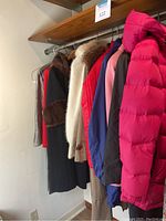 Photo showing six ladies coats and jackets hanging on a rack, various colors including red, blue, cream, dark with fur trim.
