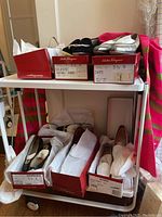 Cart with multiple Salvatore Ferragamo shoe boxes, shoes on shelves, pink and green striped shawl draped behind