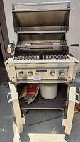 Front view of Lynx stainless steel gas grill with hood open, warming rack and rotisserie rod visible