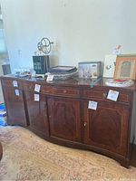 Front view of the wooden buffet showing four drawers and four cabinet doors with brass handles, placed on a patterned rug with various decorative items on top.