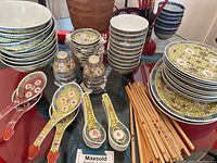 Wide view of set showing various plates, bowls, porcelain spoons, wooden chopsticks, and small tea cups arranged on table.