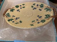 Top view of oval ceramic platter with dark blue berries and green leaves decoration.