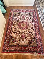Full view of vintage multi-colored rug showing central medallion, ornate floral patterns, and red border as well as frayed edge.