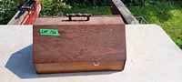 Closed view of rectangular wooden thread box with handle on top, placed outdoors on a white surface.