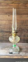 Full view of vintage Aladdin oil lamp base with tall clear glass chimney, ribbed glass base on wooden surface.