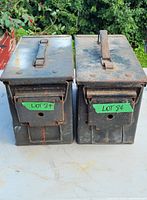 Front view of two matching weatherproof metal boxes, showing latch handles and rust spots.