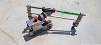 Full shot of the Laser brand chain sharpening jig showing the adjustable metal arm, clamping mechanism, and file holder on a concrete surface.