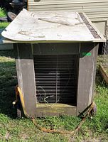 Front view of weathered insulated wooden chicken brooder box on wheels with wire mesh entry door.