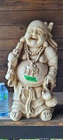 Full front view of the large Happy Buddha statue showing its joyful facial expression, beaded necklace, sack, and robe details.