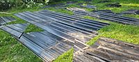 Wide view of multiple black roofing steel sheets and cutoffs laid on grass, showing size and condition