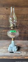 Full view of the pedestal oil lamp showing milk glass base, clear patterned glass font, and tall chimney.