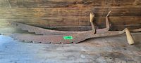 Side view of one antique hay cutter showing long serrated blade and wooden handles