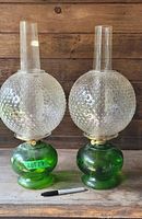 Pair of vintage oil lamps with green glass bases and clear hobnail patterned glass chimneys against wooden background.