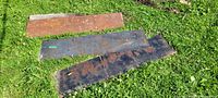 Three steel plates laid on grass showing rust and wear
