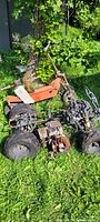 Orange scooter and small quad bike outdoors on grass, showing overall condition and layout.