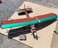 Top front view of large red and green RC gas plane with controller in background.