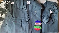 Three dark greenish coveralls laid out showing front with pockets and collar, labeled size 48, signed and made in Canada tags visible.