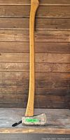 Full view of the Swedish axe leaning against a wooden backdrop showing the full wooden handle and metal head with a green label 'LOT 42'