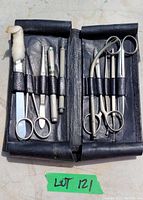 Full interior of black leather foldable case with vintage medical instruments including scissors, probes, forceps, small tube and cotton swab showing overall contents and condition.