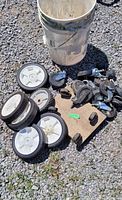 Photo of bucket with large white plastic wheels and several swivel castors on gravel surface.