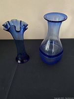 Two blue blown glass vases, one with ruffled top and gradient blue color, the other clear with blue bands and round body.